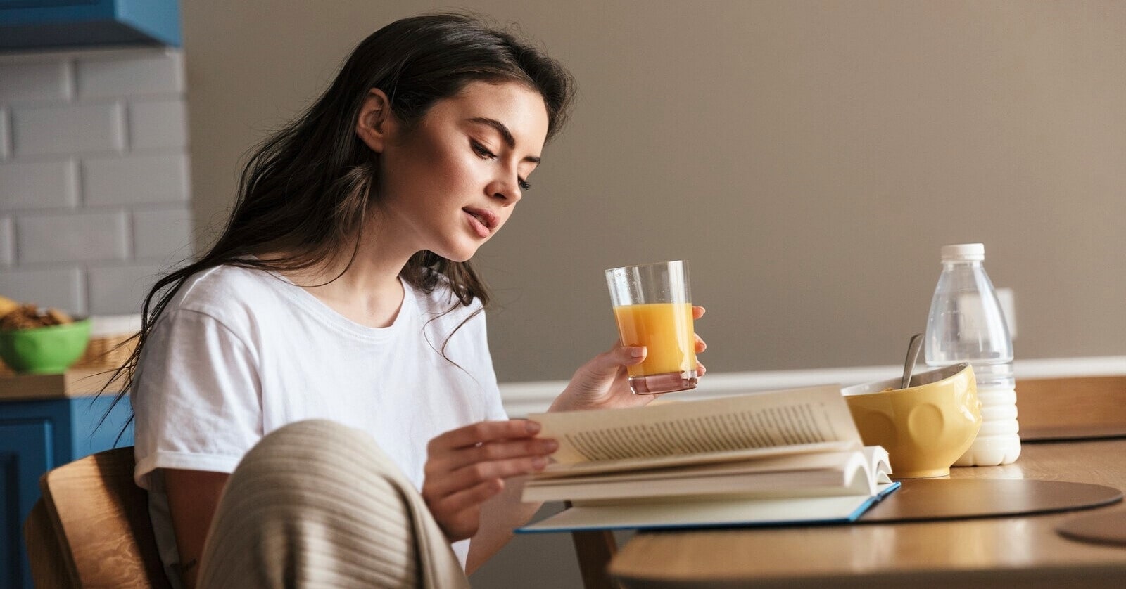 young woman sips orange juice while reading a book at the coffee table