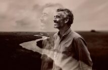 A smiling man stands in a field near a winding river, with a transparent, larger image of himself in the background, creating a dreamy, reflective atmosphere. The image is in sepia tones.